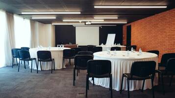 Un salón de conferencias con mesas redondas, sillas y una pantalla de proyector.