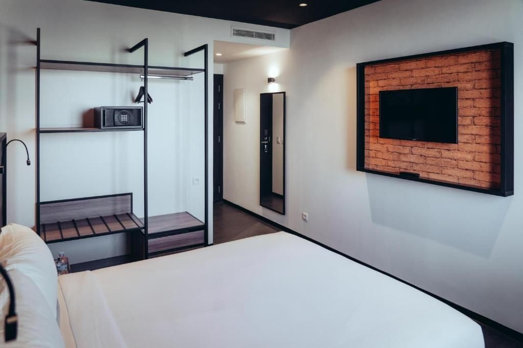 A hotel room with a bed, a TV mounted on a brick wall, a wardrobe with a mirror, and a walk-in closet.