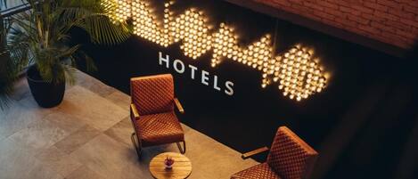 Een hotellobby met een bakstenen muur, een zithoek met twee stoelen en een tafeltje, en een kamerplant.