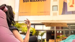 Iemand zit op een roze bank met een grote gele banner op de achtergrond.