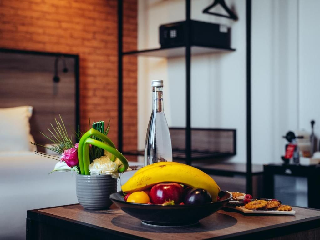 A dining table with a bowl of fruit, a bottle, and a flower arrangement.