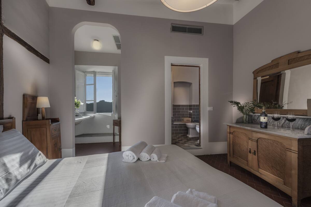 A bedroom with a large bed, a wooden dresser, a mirror, and a bathroom visible through an open door.