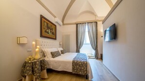 A bedroom with a large bed, a painting on the wall, a bedside table with candles, and a TV mounted on the wall. - Suite Assisi (Assisi)