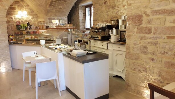 A rustic kitchen with stone walls, a central island, white cabinetry, and a dining area with chairs. - Suite Assisi (Assisi)