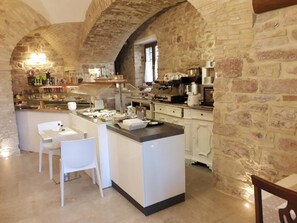 A rustic kitchen with stone walls, a central island, white cabinetry, and a dining area with chairs. - Suite Assisi (Assisi)