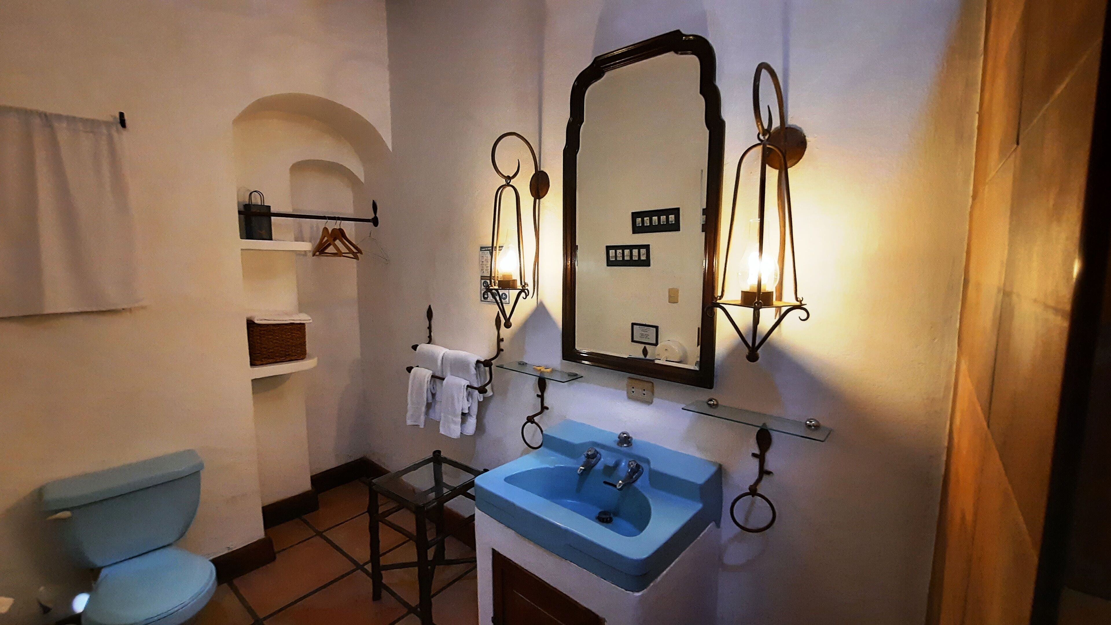 A bathroom with a toilet, a sink, and a mirror. There are shelves with towels and a hanging rack.