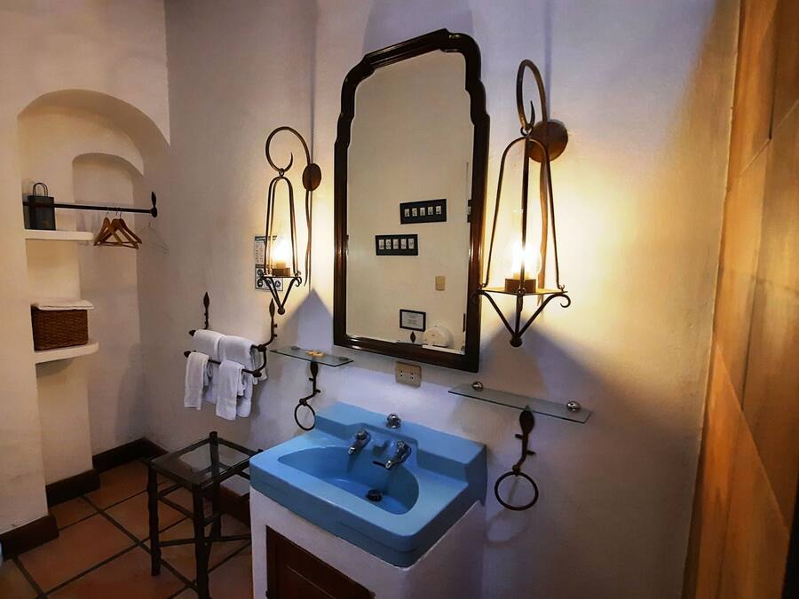 A bathroom with a toilet, a sink, and a mirror. There are shelves with towels and a hanging rack.