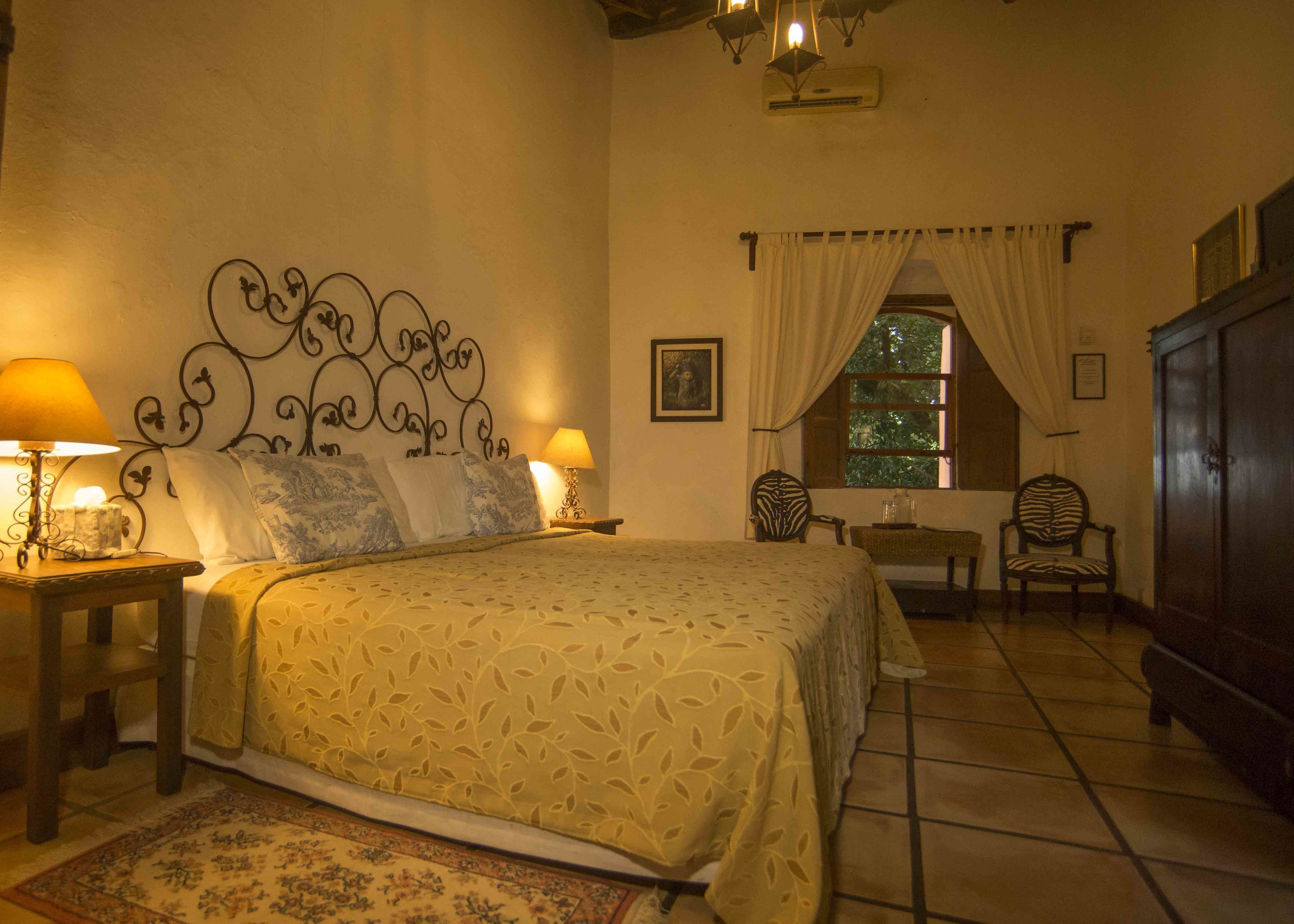 A cozy bedroom with a large bed, two bedside tables with lamps, a chair, a small table, and a wardrobe.
