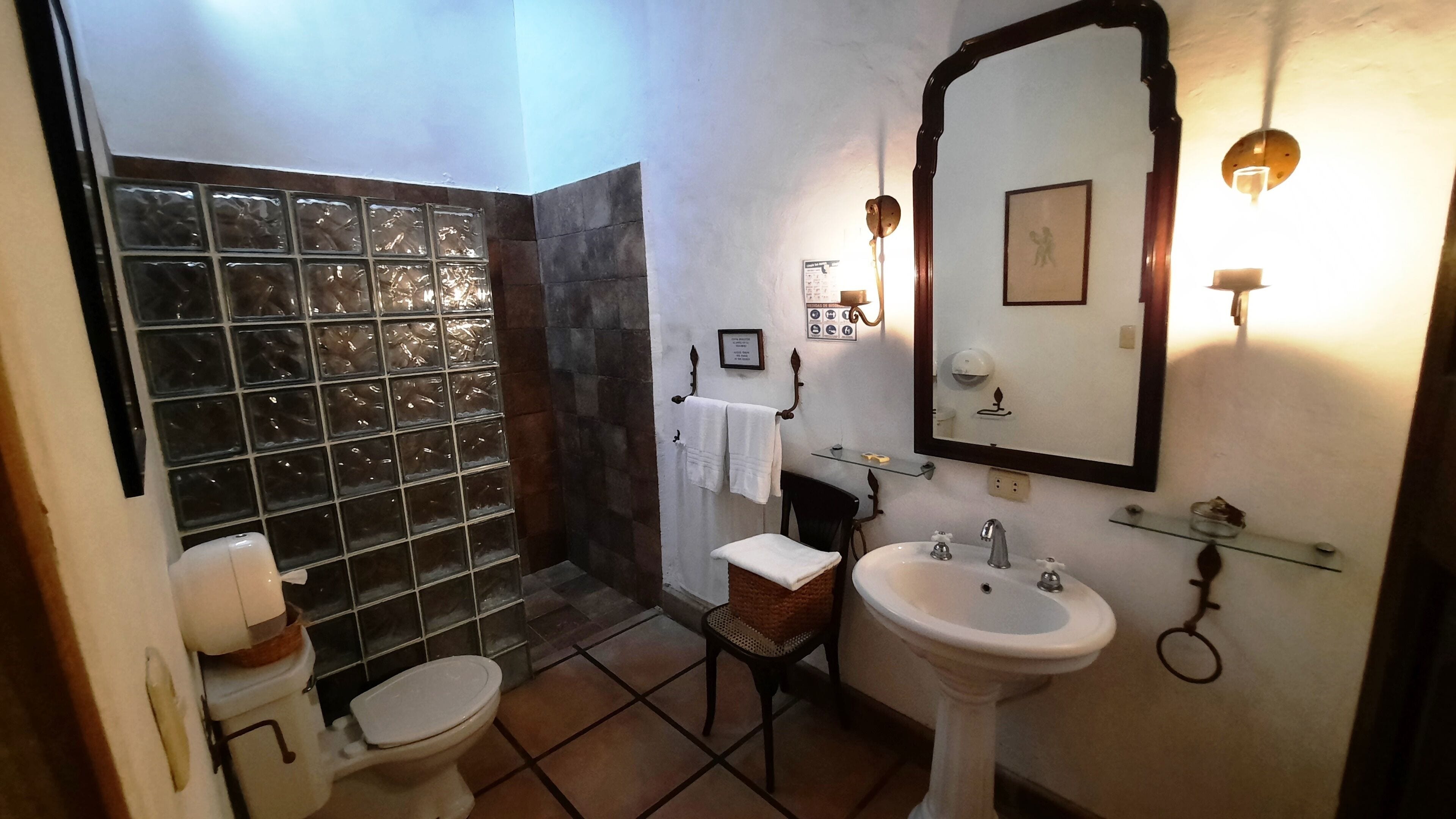 A bathroom with a glass shower enclosure, a pedestal sink, a toilet, and a vanity with a mirror.