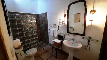 A bathroom with a glass shower enclosure, a pedestal sink, a toilet, and a vanity with a mirror.
