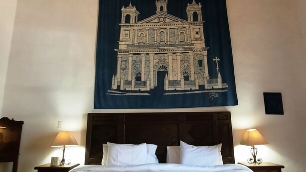 Une chambre avec un grand lit, un plafond en bois et une tapisserie représentant un bâtiment accrochée au mur.