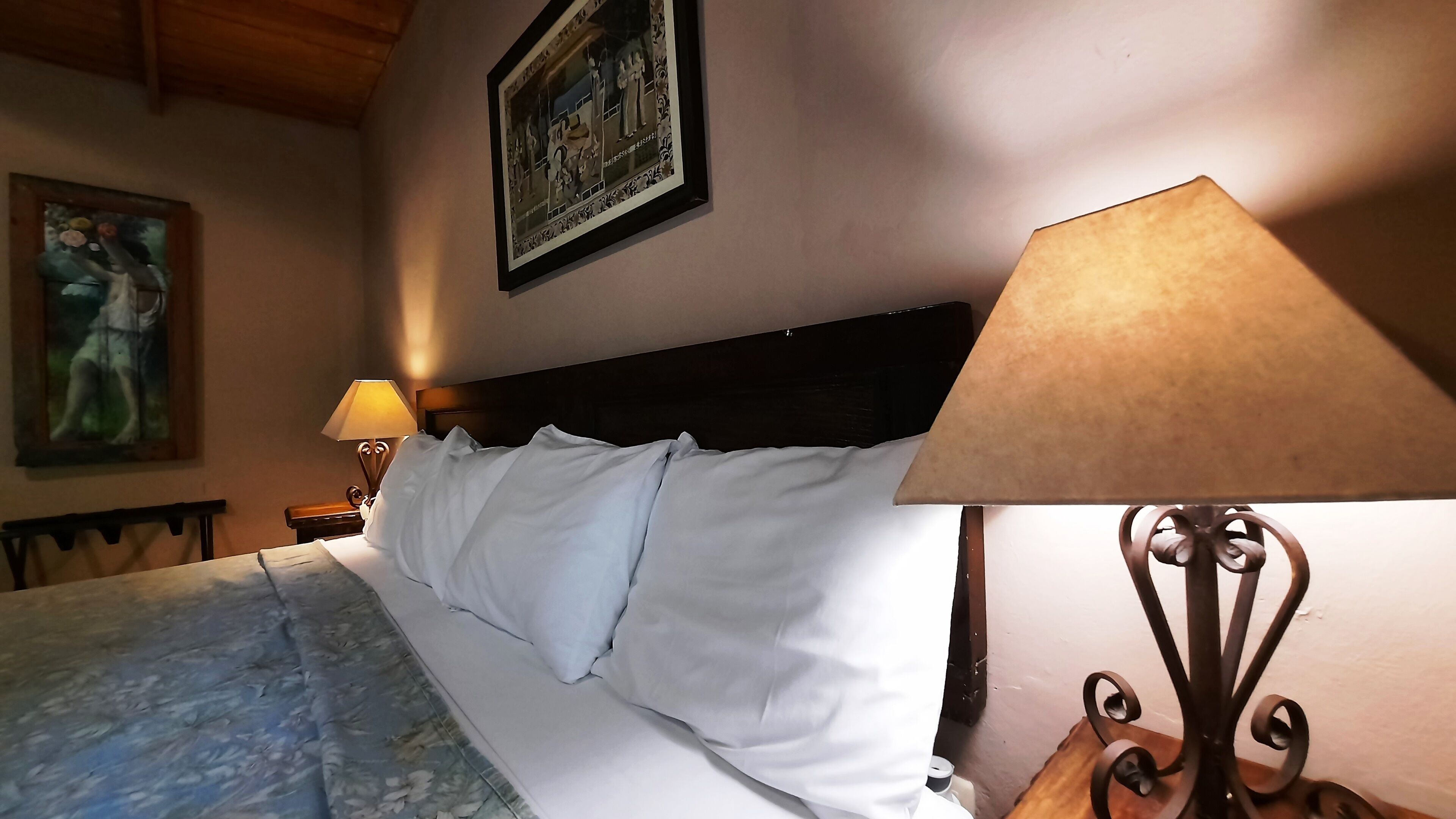 A neatly made bed with white linens, a wooden headboard, and a painting on the wall.