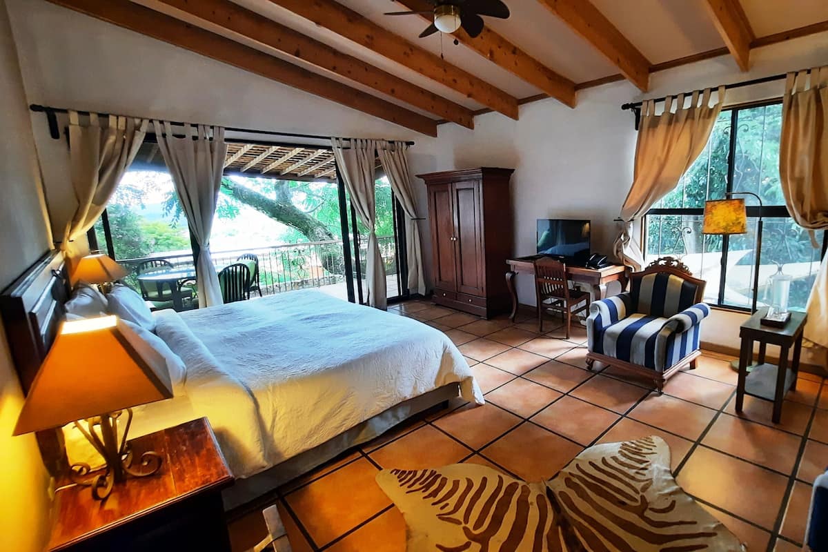 Ein Schlafzimmer mit Bett, Schreibtisch, Stuhl, Fernseher und Blick ins Freie.