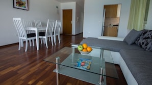Una sala de estar moderna con una mesa de centro de vidrio, un sofá gris y un comedor con sillas blancas.