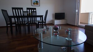 Una sala de estar moderna con una mesa de centro de vidrio, sillas de madera, un televisor de pantalla plana y un cuadro en la pared.