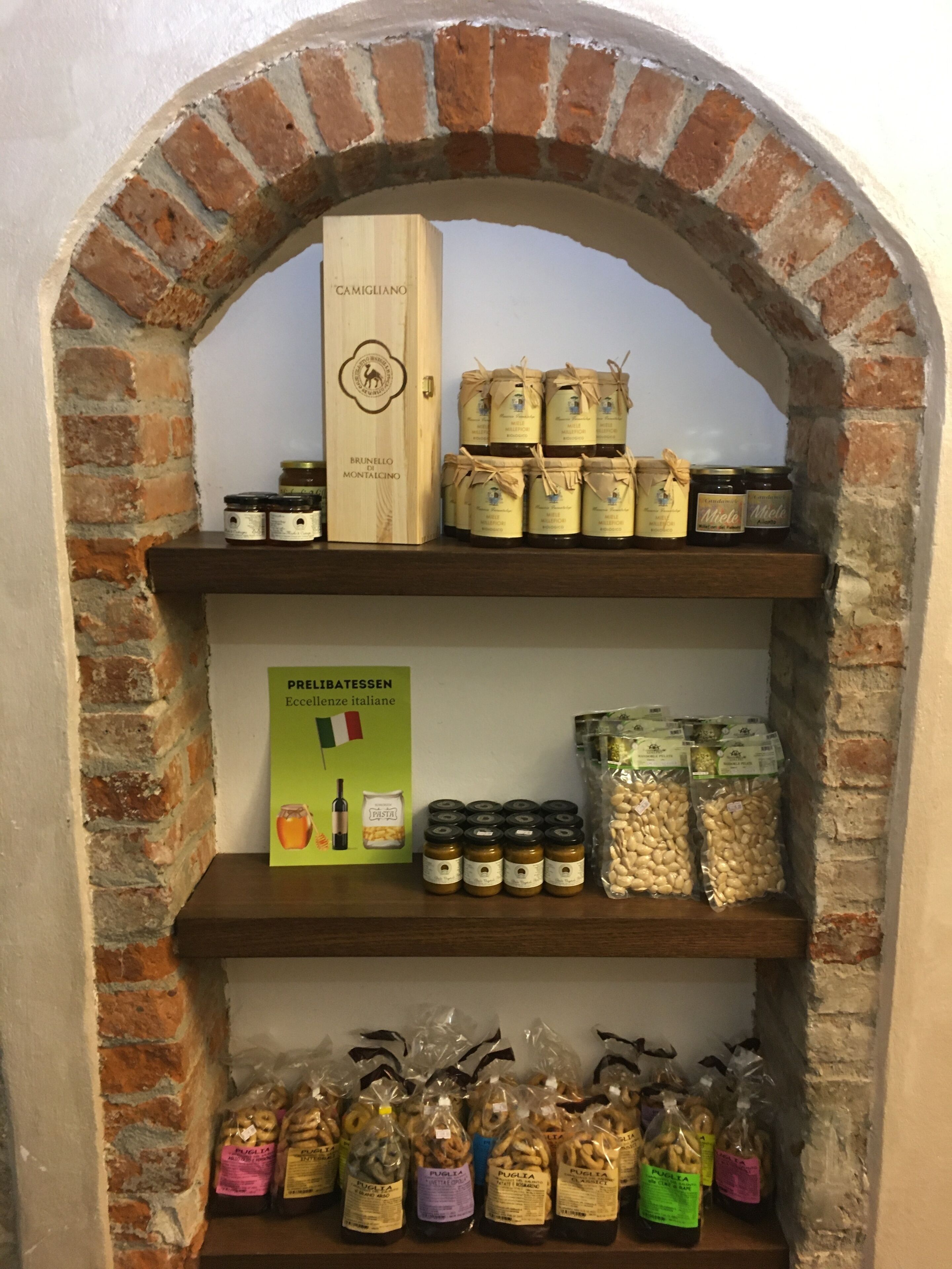 A display of food products in a brick archway, including jars of preserves, pasta, and various packaged snacks.