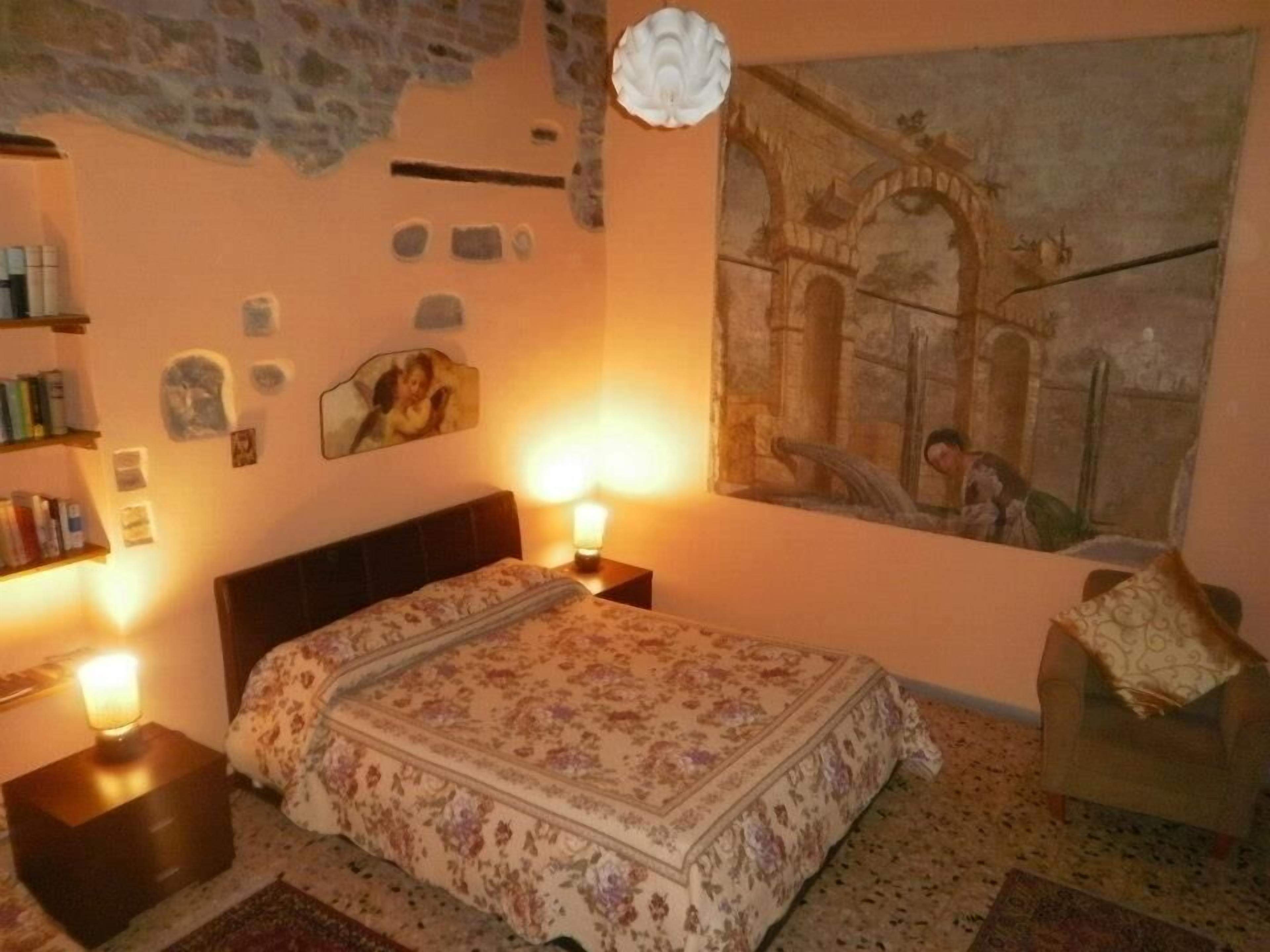 Ein Schlafzimmer mit Bett, Nachttisch, Lampe, Stuhl und einem Bild an der Wand.