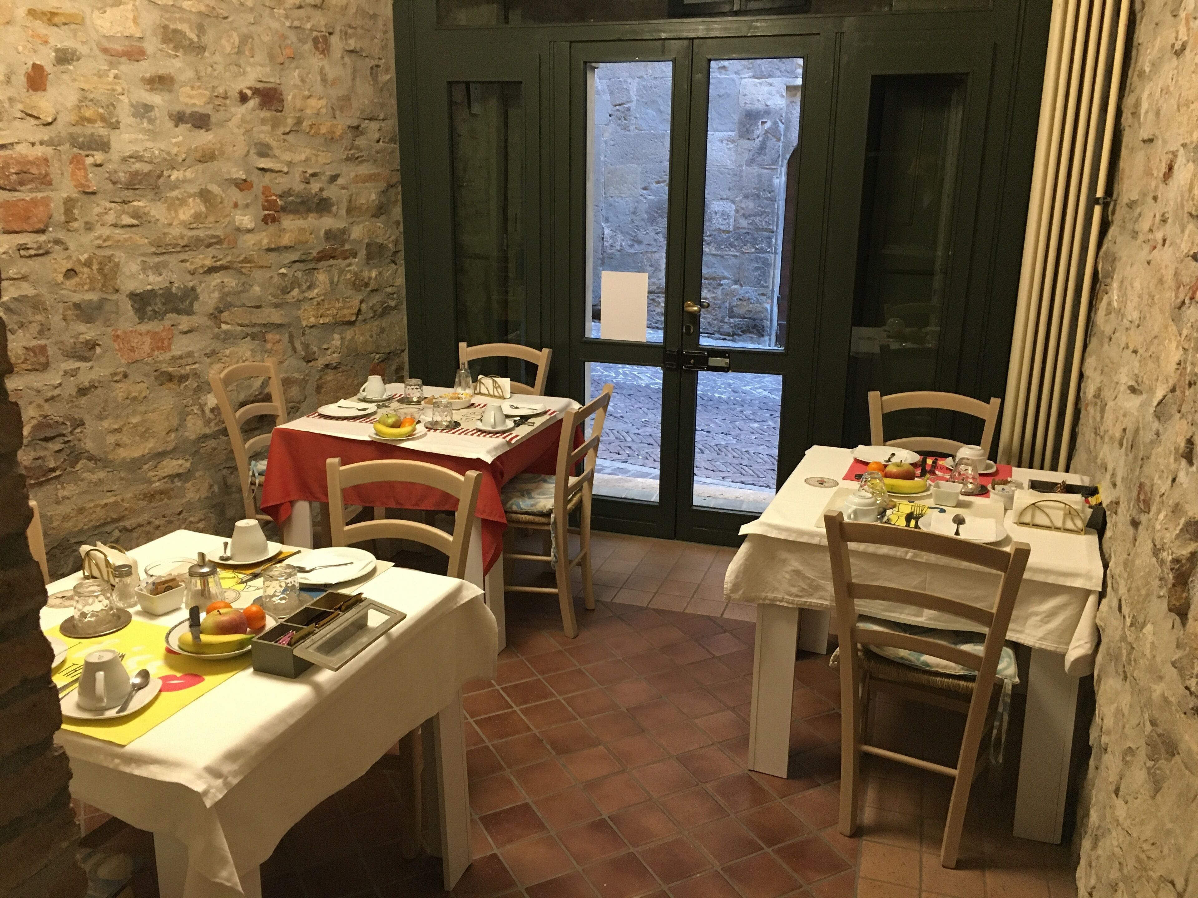 A dining area with two tables set for meals, stone walls, and a view through a glass door.