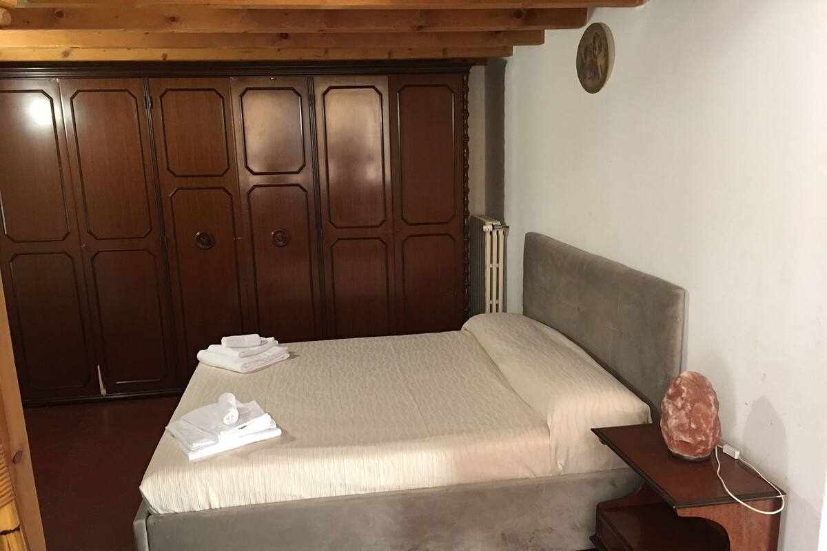 A bedroom with a bed, a wooden headboard, a bedside table with a lamp, and a radiator.