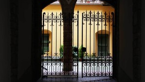 An arched doorway with a wrought iron gate leading to a building with yellow walls and green shutters. - B&B Mario Lupo (Bergamo)