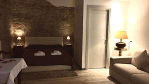 A bedroom with a stone wall, a bed with towels, bedside lamps, a door, and a sofa. - B&B Mario Lupo (Bergamo)
