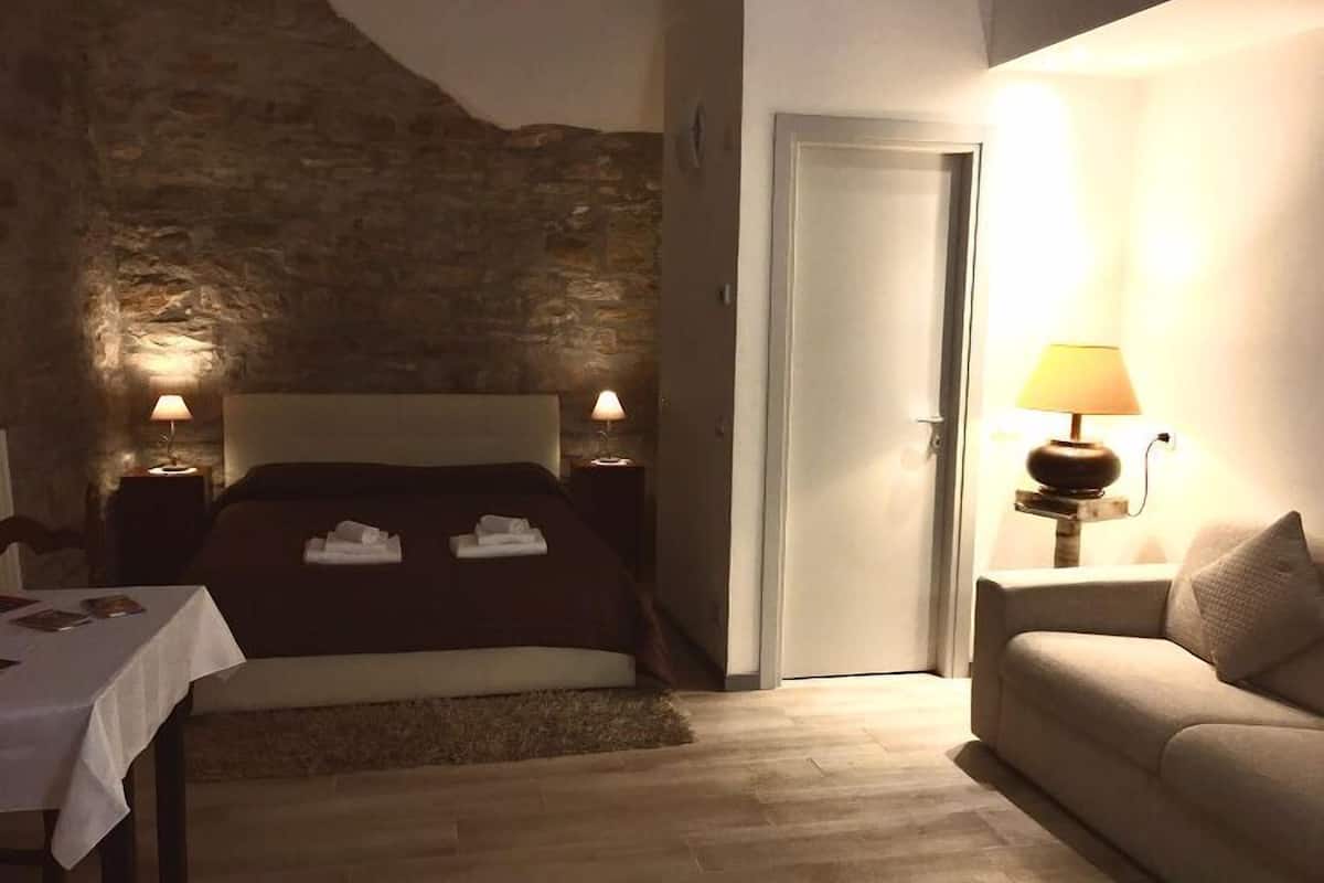 A bedroom with a stone wall, a bed with towels, bedside lamps, a door, and a sofa.