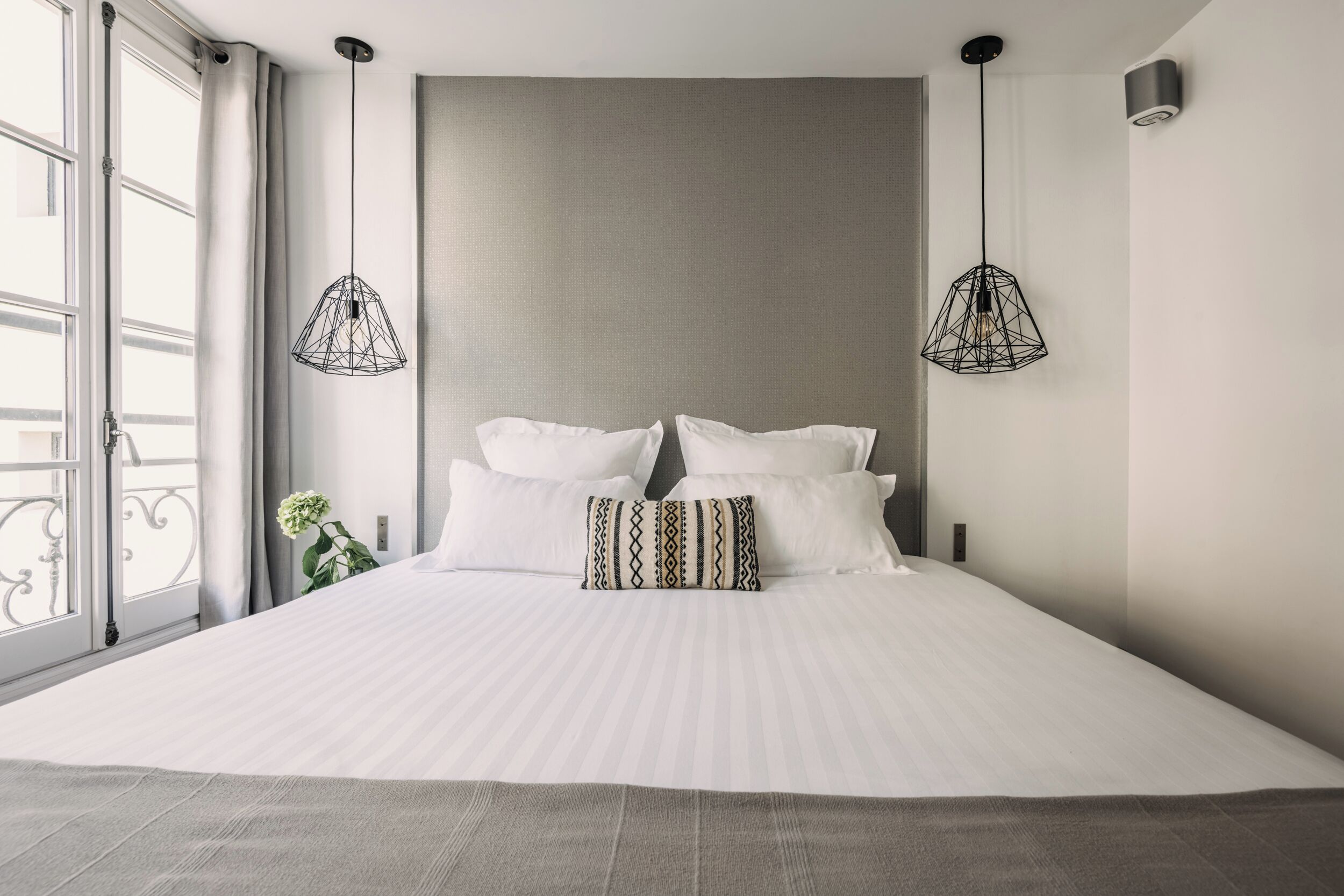 Un dormitorio moderno con una cama grande, dos lámparas colgantes y vistas al exterior.