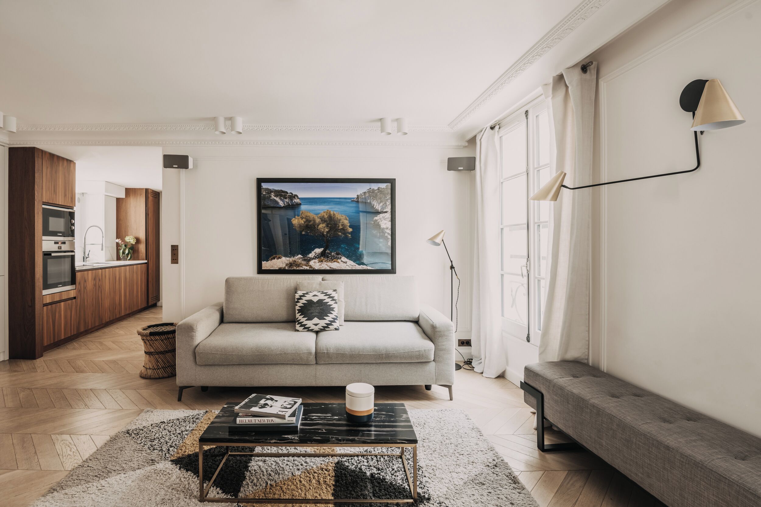A modern living room with a sofa, a coffee table, and a painting of a coastal scene.