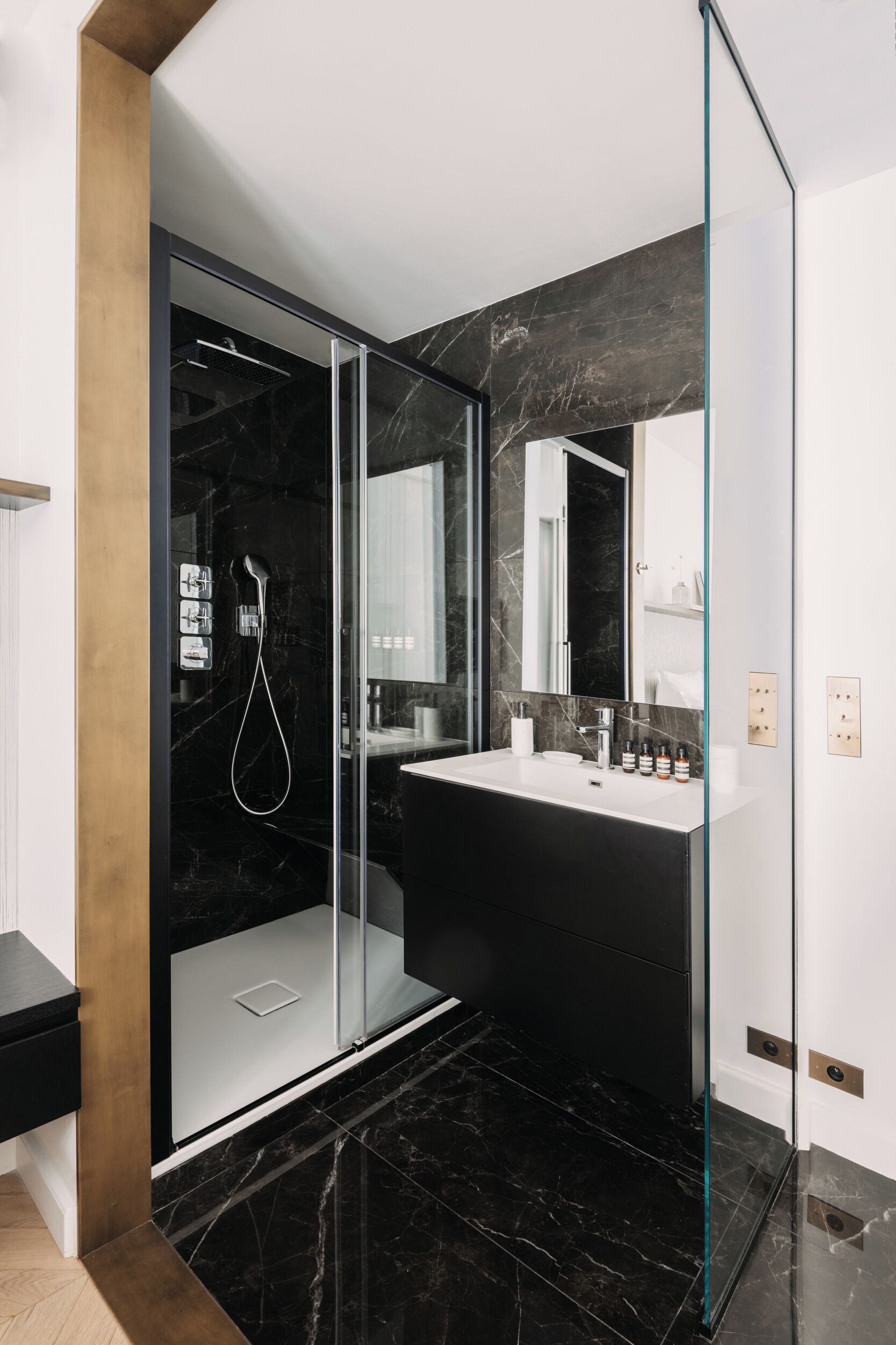 Et moderne badeværelse med en brusekabine i glas, en gulvbelægning i sort marmor og et hvidt toiletbord med et stort spejl.