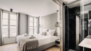 A modern bedroom with a large bed, a glass shower enclosure, and a view of the city. - HIGHSTAY - Luxury Serviced Apartments - Place Vendôme (Paris)