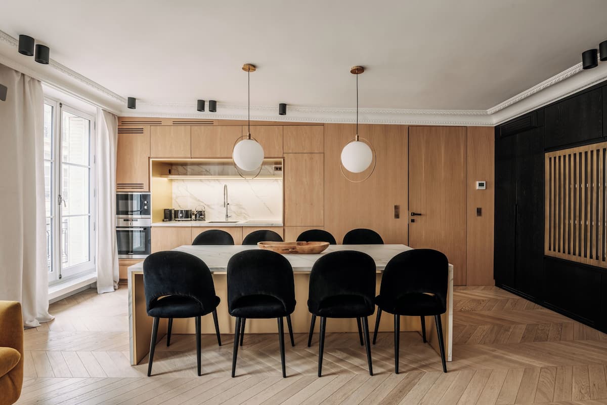 A modern kitchen with wooden cabinets, a marble countertop, and a dining area with a white table and black chairs.