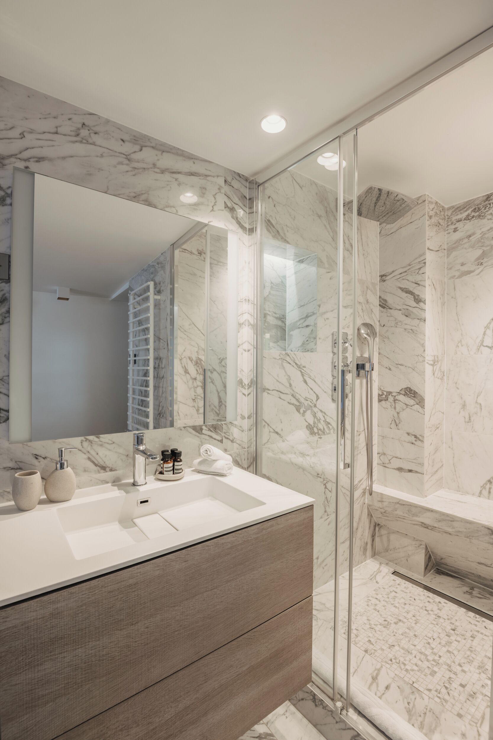 Une salle de bain moderne avec un meuble-lavabo en marbre, une cabine de douche en verre et un grand miroir.