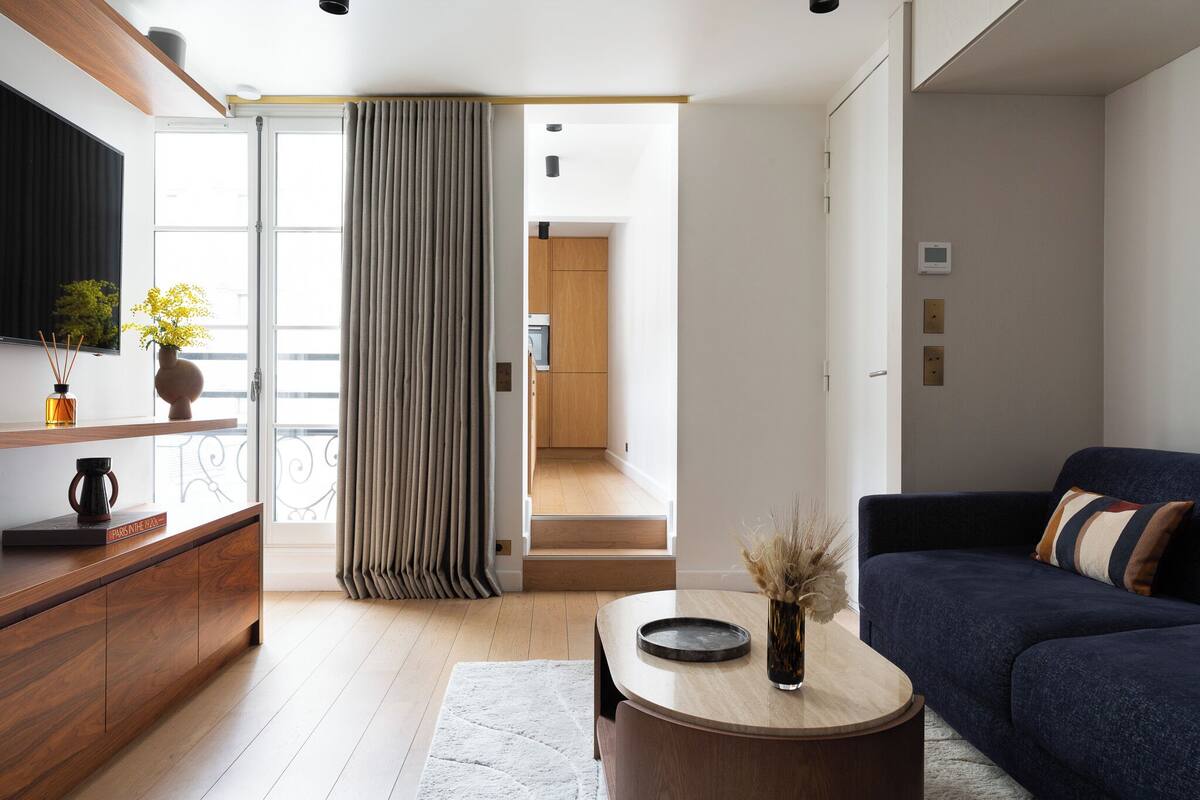 A modern living room with a dark blue sofa, a wooden coffee table, and a large window with curtains.