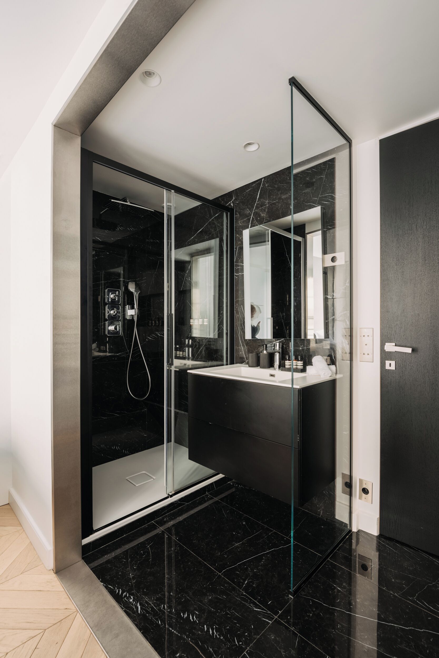 A modern bathroom with a glass-enclosed shower, a dark marble countertop, and a large mirror.