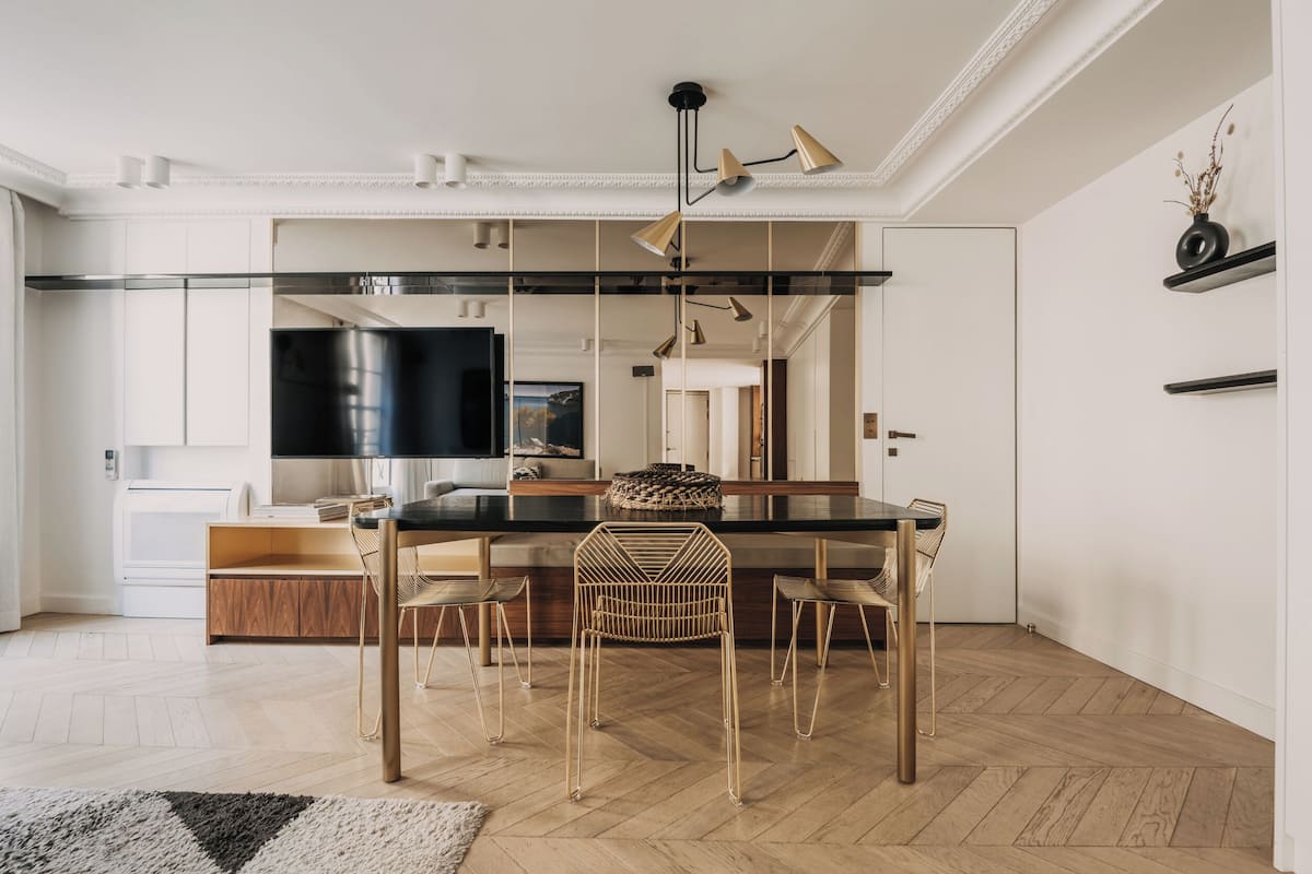 A modern kitchen with a central island, wooden chairs, and a black countertop.