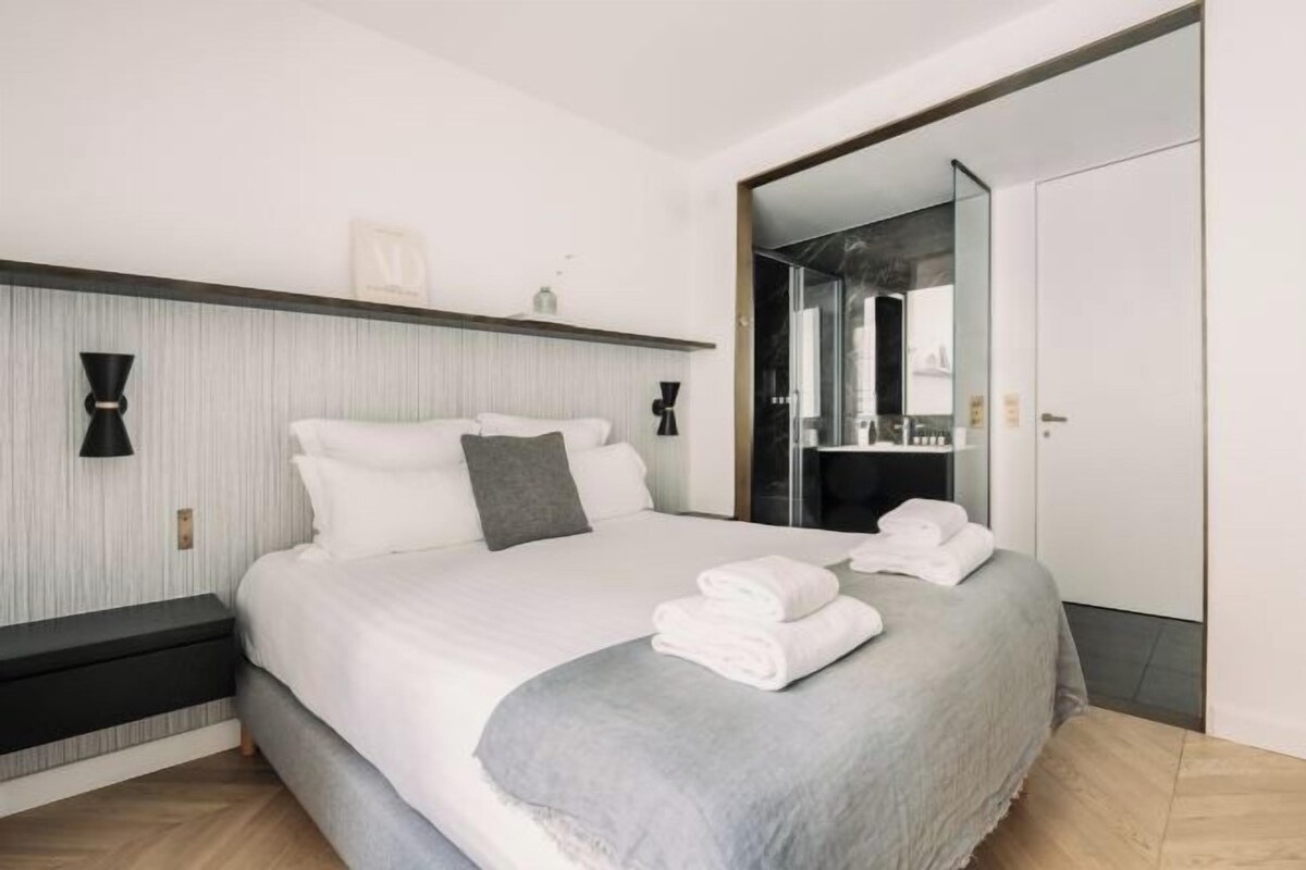 Quarto de hotel moderno com uma cama grande, mesas de cabeceira, um guarda-roupa e um espelho.