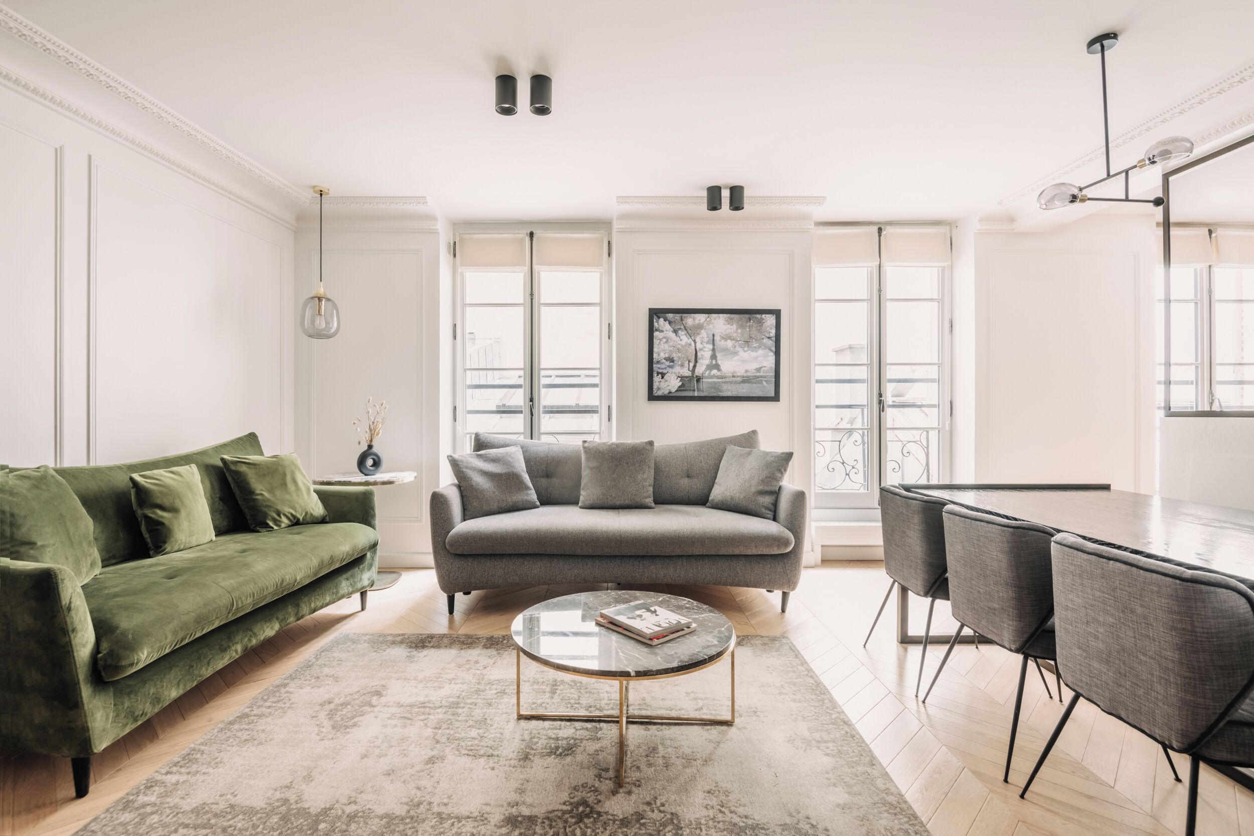Un salon moderne avec un canapé vert, une table basse ronde et un coin repas avec des chaises grises.