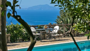 A poolside area with a view of the sea, a table with chairs, and a wooden fence. - Villa Amiela (Massa Lubrense)