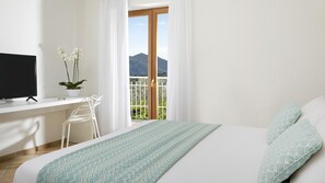 A bedroom with a bed, a desk with a computer, a potted plant, and a balcony with a mountain view. - Villa Amiela (Massa Lubrense)