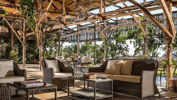 An outdoor seating area with wicker furniture, a glass-top table, and hanging lamps. - Villa Amiela (Massa Lubrense)