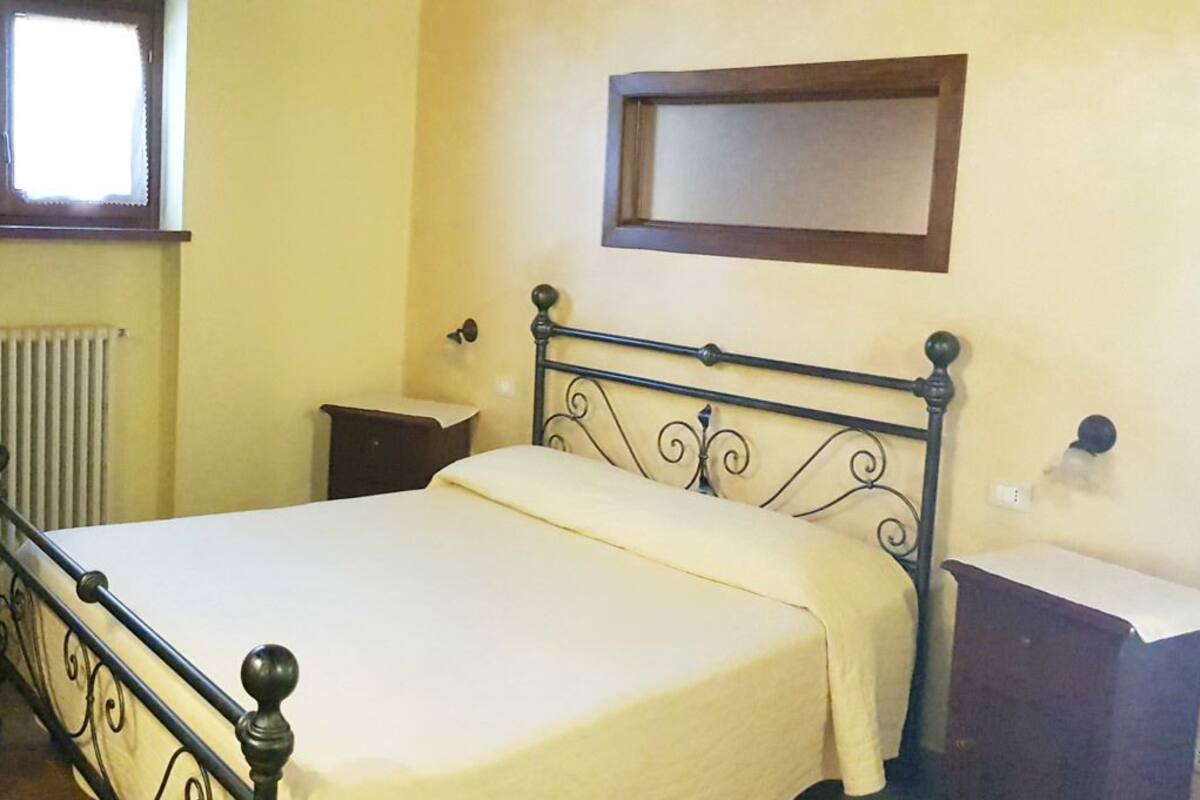 A bedroom with a single bed, a bedside table, a radiator, and a window.