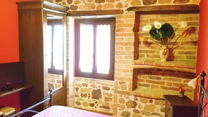Ein Zimmer mit Steinwand, einem Bett, einem Fernseher und einem Fenster mit Vorhängen.