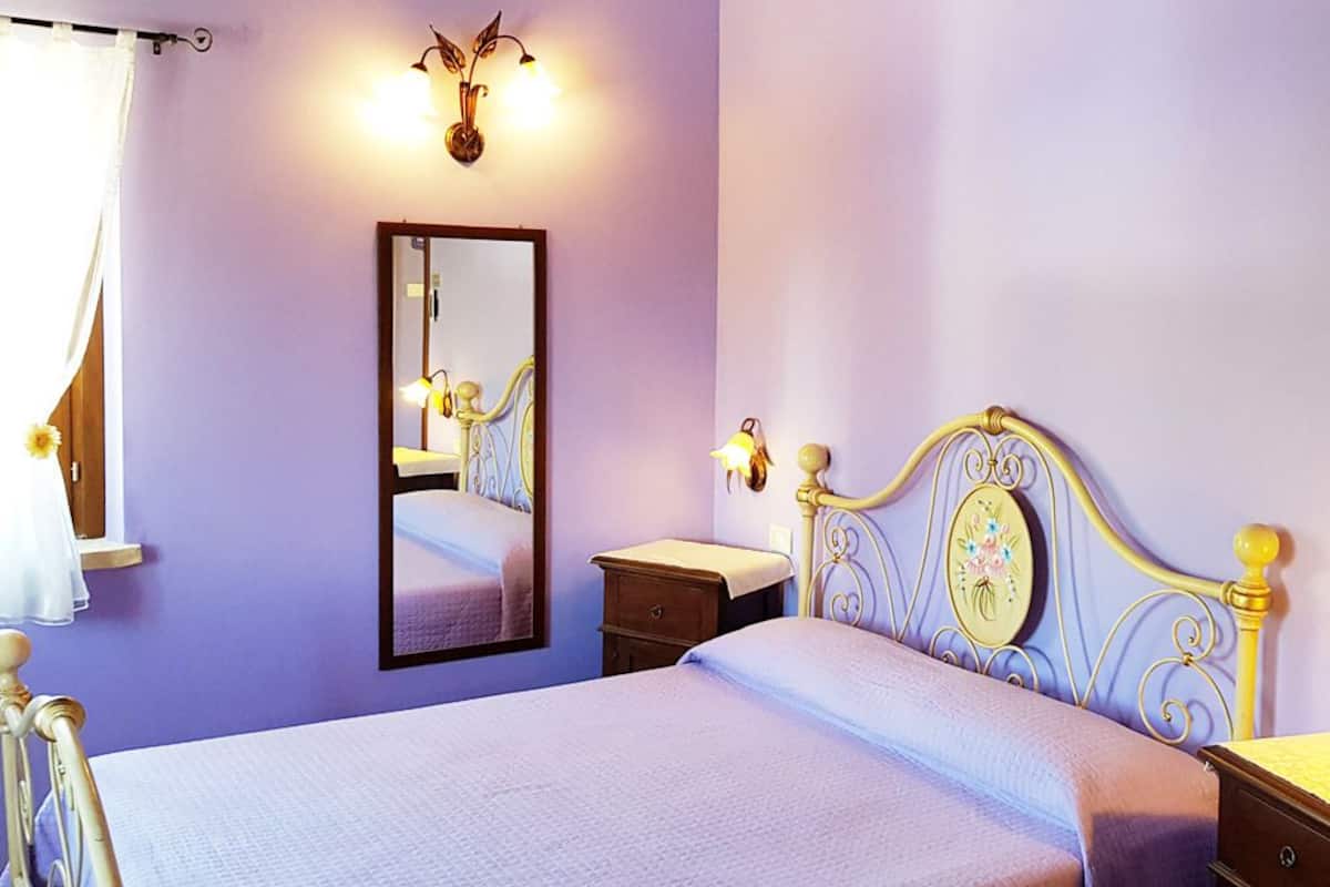 A bedroom with a bed, bedside tables, a mirror, wall sconces, and a door.