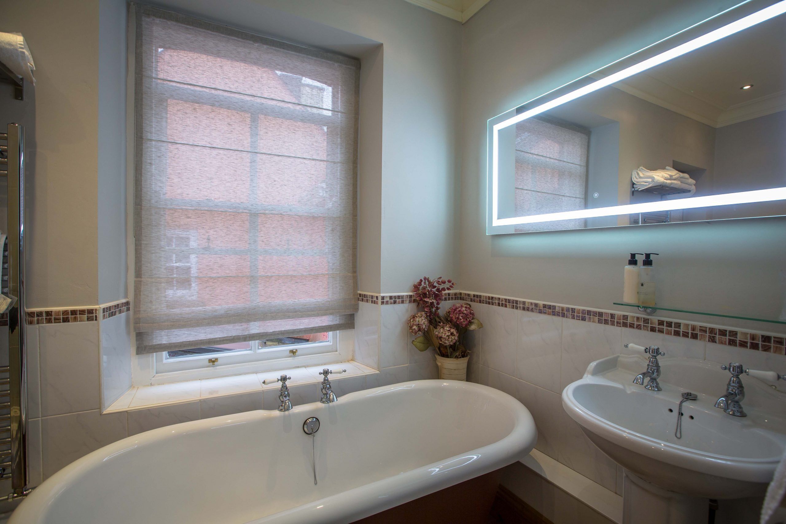 Ein Badezimmer mit Badewanne, zwei Waschbecken, einem Fenster mit Jalousien und einem Spiegel mit Beleuchtung.