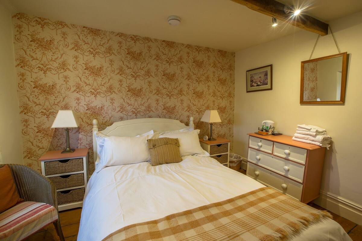A neatly arranged bedroom with a bed, two bedside tables, a chair, a dresser, and a mirror.