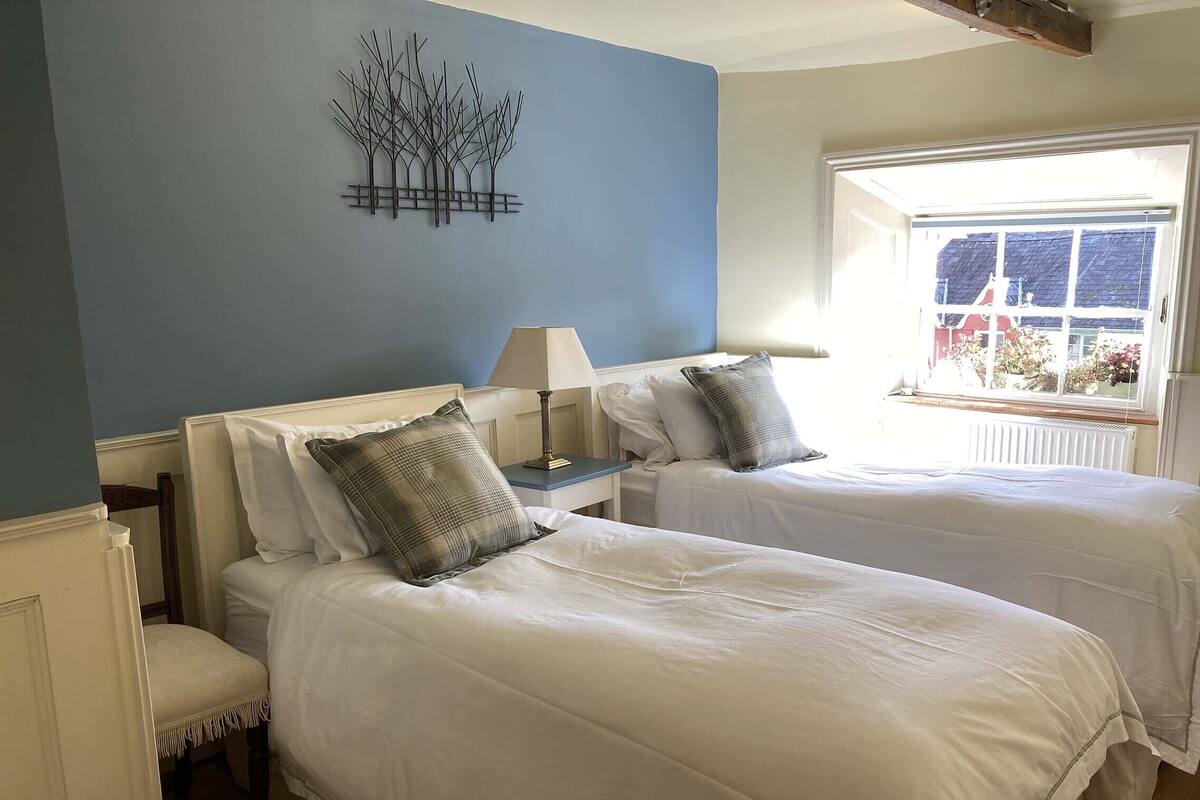 A room with two beds, a nightstand with a lamp, and a wall art piece.