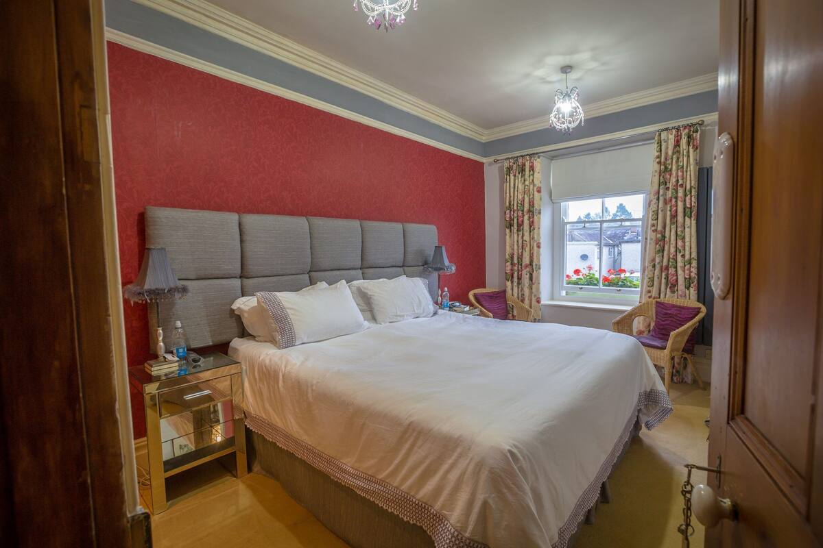 A bedroom with a large bed, a nightstand, a chair, and a window with curtains.