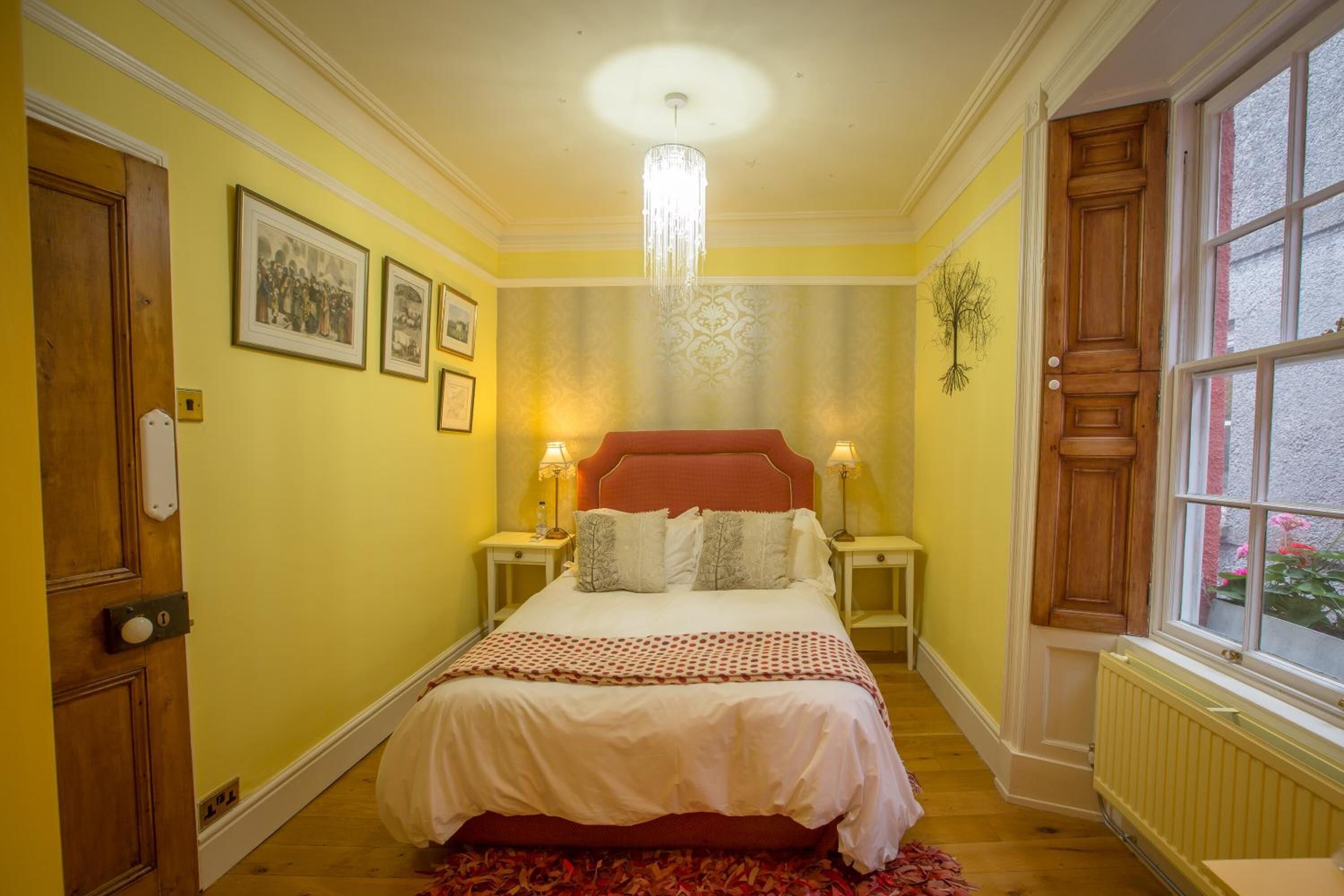 A bedroom with a large bed, wooden doors, a chandelier, and framed pictures on the wall.