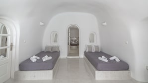 Ein schlicht eingerichtetes Zimmer mit zwei Betten, einem durch einen Bogen sichtbaren Badezimmer und einem Flur, der zu einem weiteren Zimmer führt.