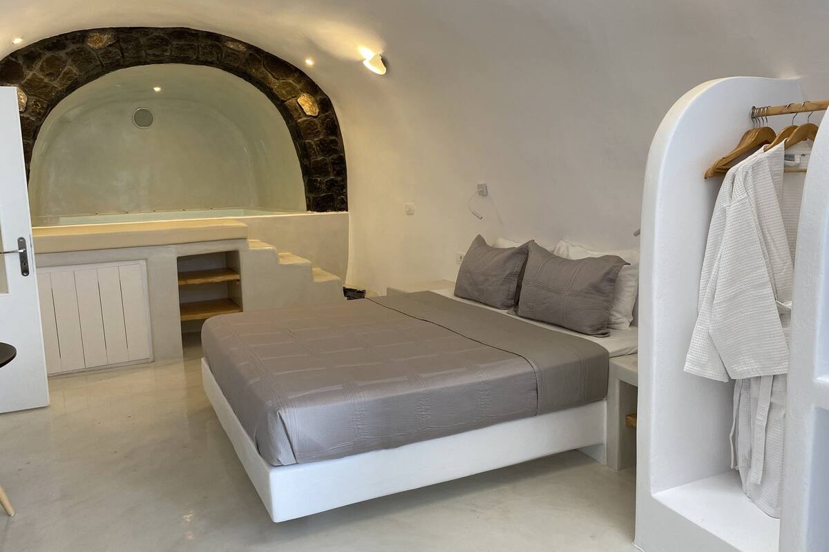 A modern bedroom with a built-in bathtub, a vanity with a stone arch, and a bed with grey bedding.
